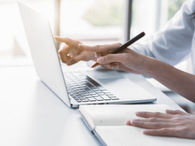 Close up of two businesswoman using laptop and writing on notebook in the morning. Business and financial concept. People and lifestyles concept. Office and workplace theme.