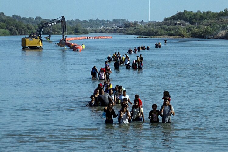 2023년 7월 27일 텍사스주 이글 패스로 진입하기 위해 와이어의 구멍을 찾으면서 리오 그란데 강을 건너는 이민자들. 로이터