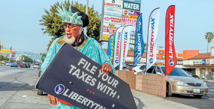 세금보고 시즌을 알리는 리버티 택스 ‘웨이버’가 LA한인타운 웨스턴 애비뉴에서 가게 안내 표지판을 들고 홍보 활동을 벌이고 있다. 김상진 기자