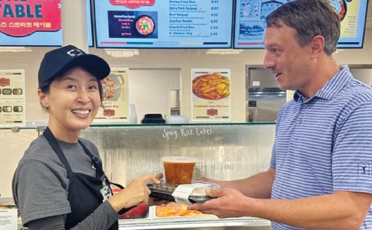 크로거 마켓 휴스턴 지점에 개장한 한식 델리 ‘라이언스 스트리트 테이블’의 스테이시 권(왼쪽) 대표가 백인 고객에게 김치찌개와 반찬을 건네고 있다. [라이언스 스트리트 테이블 제공]